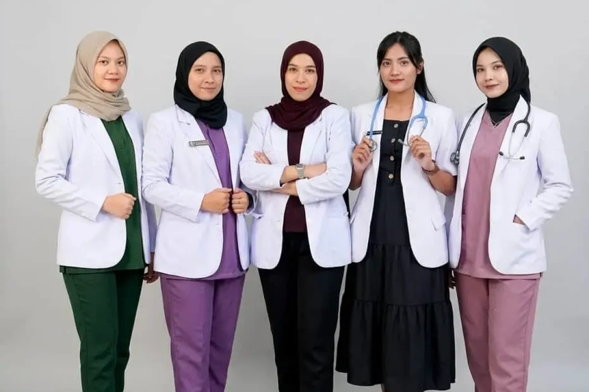 Lima wanita berhijab mengenakan jas lab putih dan seragam medis, berdiri di depan latar belakang abu-abu.
